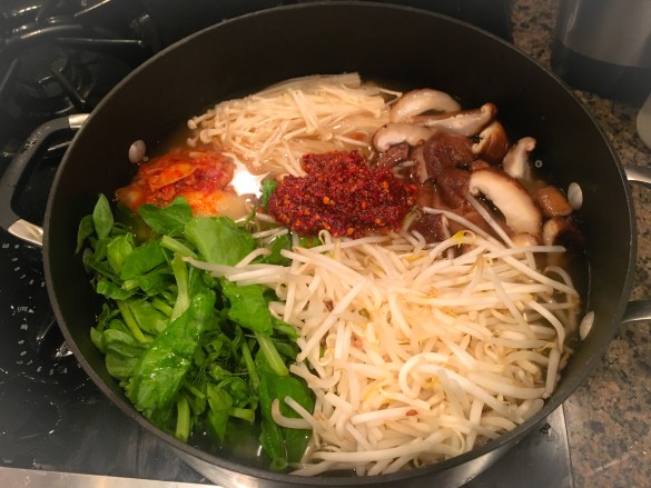 Budae Jjigae starting with chicken broth, sauce, tofu, sprouts, pea shoots, enoki mushrooms, and shittake mushrooms, and kimchi